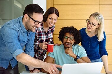 Team of diverse professionals collaborating on a laptop in a modern office, discussing digital marketing strategies